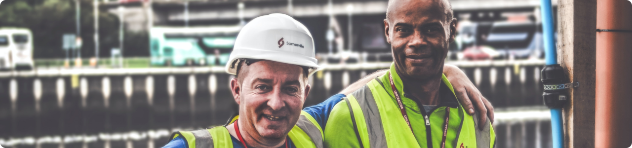 A male construction worker smiling with his arm wrapped around a colleague.