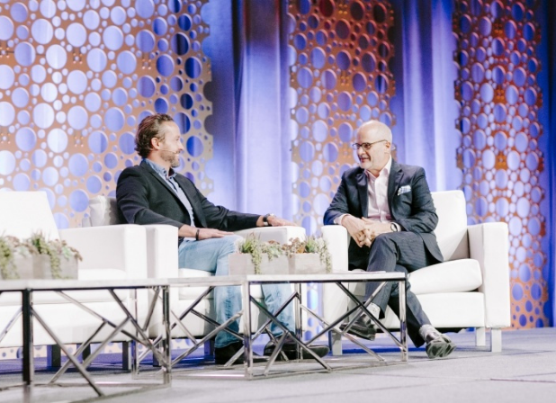 Jeff Shore sits on a stage talking with a business man