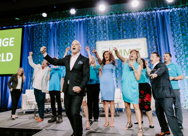 Jeff Shore stands on a stage with an enthusiastic group cheering behind him