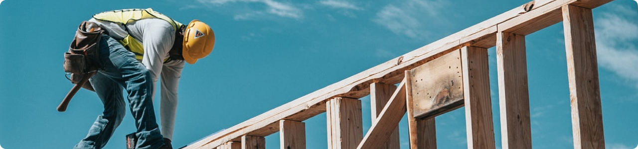 A man nailing the wooden frame of a home.