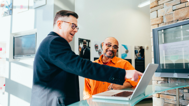 A man in a suit pointing at a laptop to another man.