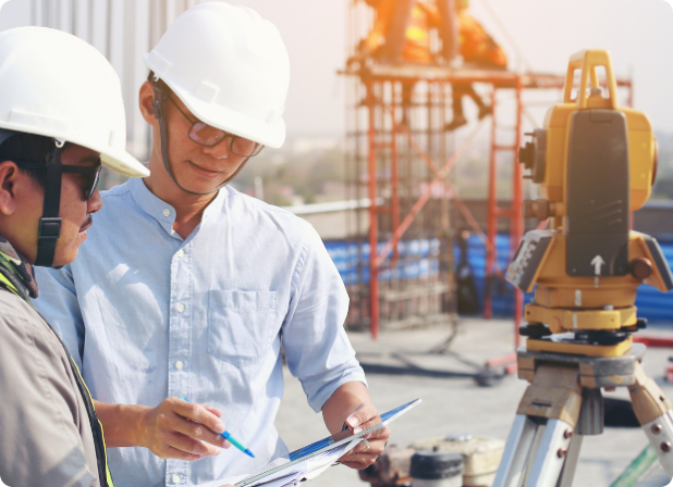 A man in a hard hat pointing with a pen towards a tablet to another man.